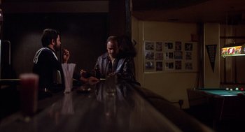 Movie still from “When a Stranger Calls” (1979), directed by Fred Walton – Two men are sitting at a bar and one of them has a cigarette in his mouth; Wide shot, Over the shoulder angle