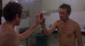 Movie still from “When a Stranger Calls” (1979), directed by Fred Walton – A shirtless man holding his hands up in front of a mirror; Close Up shot, Low angle