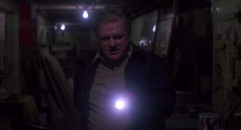 Movie still from “When a Stranger Calls” (1979), directed by Fred Walton – A man holding a flashlight in a dark room; Medium shot, Low angle