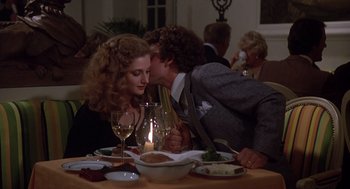 A man and a woman sitting at a dinner table kissing