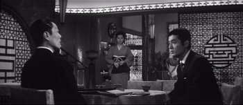 Movie still from “When a Woman Ascends the Stairs” (1960), directed by Mikio Naruse – A black and white photo of a woman standing in front of two men; Medium shot, Low angle