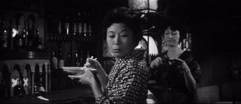 Movie still from “When a Woman Ascends the Stairs” (1960), directed by Mikio Naruse – A woman is holding a bowl of food in her hands; Medium shot, Low angle