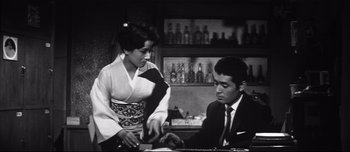 Movie still from “When a Woman Ascends the Stairs” (1960), directed by Mikio Naruse – A woman in a kimono and a man in a suit and tie in front of a bar; Medium shot, Low angle