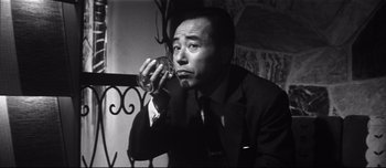 Movie still from “When a Woman Ascends the Stairs” (1960), directed by Mikio Naruse – A man in a suit and tie drinking a glass of wine; Close Up shot, Low angle