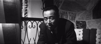 Movie still from “When a Woman Ascends the Stairs” (1960), directed by Mikio Naruse – A man in a suit and tie sitting in front of a railing; Close Up shot, Low angle