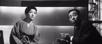 Movie still from “When a Woman Ascends the Stairs” (1960), directed by Mikio Naruse – A man and a woman are standing next to each other in front of a wall; Medium shot, Low angle