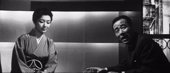 Movie still from “When a Woman Ascends the Stairs” (1960), directed by Mikio Naruse – A man and a woman sitting in front of a wall; Medium shot, Over the shoulder angle