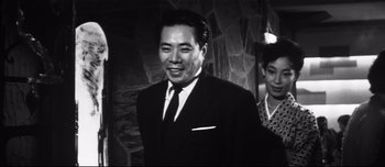 Movie still from “When a Woman Ascends the Stairs” (1960), directed by Mikio Naruse – An old photo of a man in a suit and tie; Medium shot, Low angle