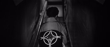 Movie still from “When a Woman Ascends the Stairs” (1960), directed by Mikio Naruse – A person with a backpack walking down a flight of stairs; Medium shot, Overhead angle