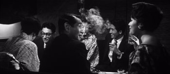 Movie still from “When a Woman Ascends the Stairs” (1960), directed by Mikio Naruse – A black and white photo of a group of people sitting at a table; Medium shot, Over the shoulder angle