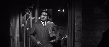 Movie still from “When a Woman Ascends the Stairs” (1960), directed by Mikio Naruse – A black and white photo of a man in a suit and tie; Medium shot, Low angle