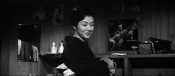 Movie still from “When a Woman Ascends the Stairs” (1960), directed by Mikio Naruse – An asian woman holding a book in her hands; Medium shot, Low angle