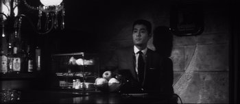 Movie still from “When a Woman Ascends the Stairs” (1960), directed by Mikio Naruse – A black and white photo of a man sitting at a table; Medium shot, Low angle