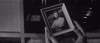 Movie still from “When a Woman Ascends the Stairs” (1960), directed by Mikio Naruse – A person holding up a picture frame with a picture of a man in it; Extreme Close Up shot, Low angle
