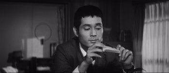 Movie still from “When a Woman Ascends the Stairs” (1960), directed by Mikio Naruse – A black - and - white photo of a man eating a sandwich; Close Up shot, High angle