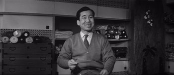 Movie still from “When a Woman Ascends the Stairs” (1960), directed by Mikio Naruse – An old photo of a man smiling for the camera; Medium shot, Low angle
