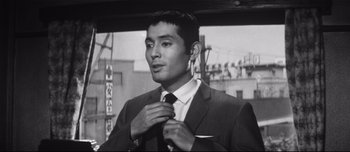 Movie still from “When a Woman Ascends the Stairs” (1960), directed by Mikio Naruse – Black and white photograph of a man adjusting his tie; Close Up shot, Low angle