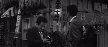 Movie still from “When a Woman Ascends the Stairs” (1960), directed by Mikio Naruse – Two men in business suits standing next to each other; Medium shot, Low angle