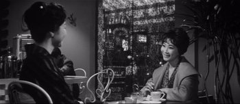 Movie still from “When a Woman Ascends the Stairs” (1960), directed by Mikio Naruse – A black and white photo of a woman sitting at a table; Medium shot, High angle