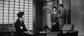 Movie still from “When a Woman Ascends the Stairs” (1960), directed by Mikio Naruse – A man and a woman standing in front of another man; Medium shot, Over the shoulder angle