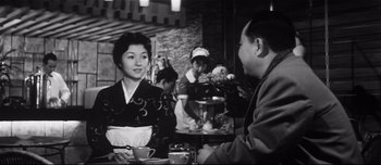 Movie still from “When a Woman Ascends the Stairs” (1960), directed by Mikio Naruse – An old photo of two people sitting at a table; Medium shot, Over the shoulder angle