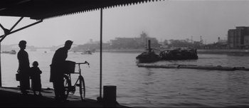 Movie still from “When a Woman Ascends the Stairs” (1960), directed by Mikio Naruse – A bicycle parked on the side of a river near a boat; Extreme Wide shot, Low angle