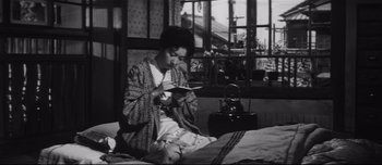 Movie still from “When a Woman Ascends the Stairs” (1960), directed by Mikio Naruse – A woman sitting on a bed looking at her phone; Medium shot, High angle