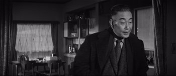 Movie still from “When a Woman Ascends the Stairs” (1960), directed by Mikio Naruse – An older man wearing a suit and tie in a living room; Close Up shot, Low angle
