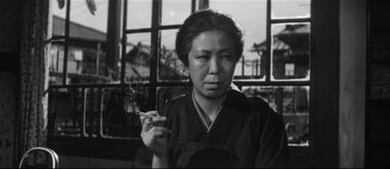 Movie still from “When a Woman Ascends the Stairs” (1960), directed by Mikio Naruse – An older woman smoking a cigarette in front of a window; Close Up shot, Low angle