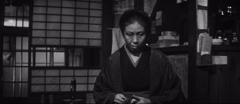 Movie still from “When a Woman Ascends the Stairs” (1960), directed by Mikio Naruse – An older woman in a kimono looking down at a piece of paper; Medium shot, Low angle
