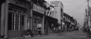 Movie still from “When a Woman Ascends the Stairs” (1960), directed by Mikio Naruse – A man walking down the street in front of a building; Wide shot, Low angle