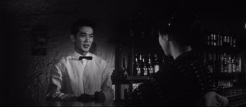 Movie still from “When a Woman Ascends the Stairs” (1960), directed by Mikio Naruse – A man in a white shirt is talking to a woman in a black dress; Medium shot, Low angle