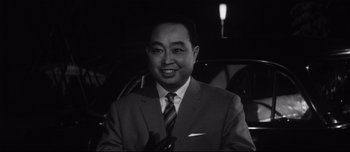 Movie still from “When a Woman Ascends the Stairs” (1960), directed by Mikio Naruse – Black and white photograph of a man in a suit and tie; Close Up shot, Low angle