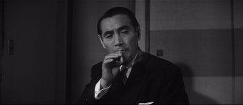 Movie still from “When a Woman Ascends the Stairs” (1960), directed by Mikio Naruse – A man in a suit and tie smoking a cigarette; Close Up shot, Low angle