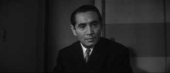 Movie still from “When a Woman Ascends the Stairs” (1960), directed by Mikio Naruse – An old black and white photo of a man wearing a suit; Close Up shot, Low angle