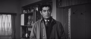 Movie still from “When a Woman Ascends the Stairs” (1960), directed by Mikio Naruse – A black and white photo of a man wearing a coat; Close Up shot, Low angle