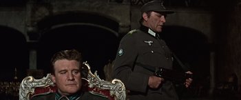Movie still from “Where Eagles Dare” (1968), directed by Brian G. Hutton – A man in a military uniform standing next to another man in a suit; Medium shot, Low angle