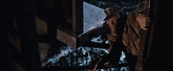 Movie still from “Where Eagles Dare” (1968), directed by Brian G. Hutton – A man in a hat is using a chain saw to cut a tree; Medium shot, Low angle