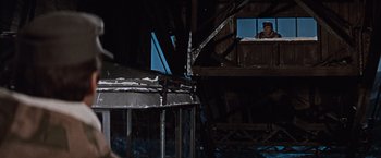 Movie still from “Where Eagles Dare” (1968), directed by Brian G. Hutton – A man standing on top of a metal structure next to a building; Wide shot, Low angle