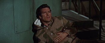 Movie still from “Where Eagles Dare” (1968), directed by Brian G. Hutton – A man in a raincoat is sitting on the ground; Close Up shot, High angle
