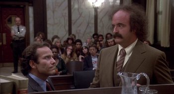 Movie still from “Where the Buffalo Roam” (1980), directed by Art Linson – Two men in suits and ties in front of a group of onlookers in a courtroom; Medium shot, Low angle
