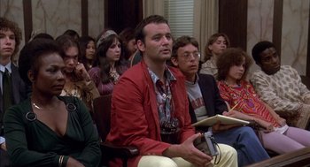 Movie still from “Where the Buffalo Roam” (1980), directed by Art Linson – A group of people sitting in front of a crowd; Medium shot, High angle
