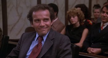 Movie still from “Where the Buffalo Roam” (1980), directed by Art Linson – A man sitting in front of other people in a room; Close Up shot, Low angle