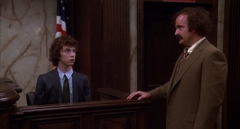 Movie still from “Where the Buffalo Roam” (1980), directed by Art Linson – A man in a suit and tie standing in front of a judge; Medium shot, Over the shoulder angle