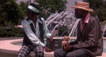 Movie still from “Where the Buffalo Roam” (1980), directed by Art Linson – A couple of men sitting next to each other on top of a bench; Medium shot, Low angle