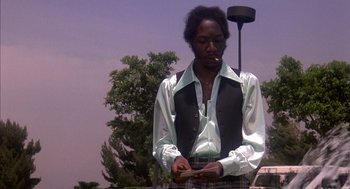 Movie still from “Where the Buffalo Roam” (1980), directed by Art Linson – A man smoking a cigarette while standing outside; Medium shot, Low angle