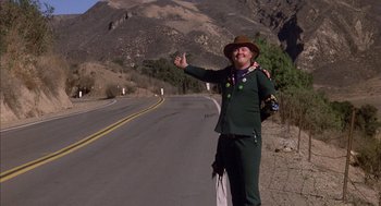 Movie still from “Where the Buffalo Roam” (1980), directed by Art Linson – A man in a green suit standing on the side of a road; Wide shot, Low angle