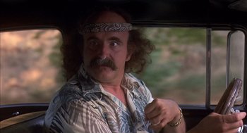 Movie still from “Where the Buffalo Roam” (1980), directed by Art Linson – A man with long curly hair and a bandana on his head driving a car; Close Up shot, Low angle
