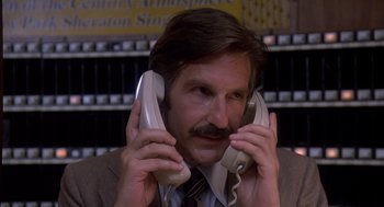 Movie still from “Where the Buffalo Roam” (1980), directed by Art Linson – A man in a suit and tie holding a pair of phones to his ears; Close Up shot, Low angle