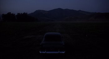 Movie still from “Where the Buffalo Roam” (1980), directed by Art Linson – The back of a car parked in a field at night; Extreme Wide shot, High angle
